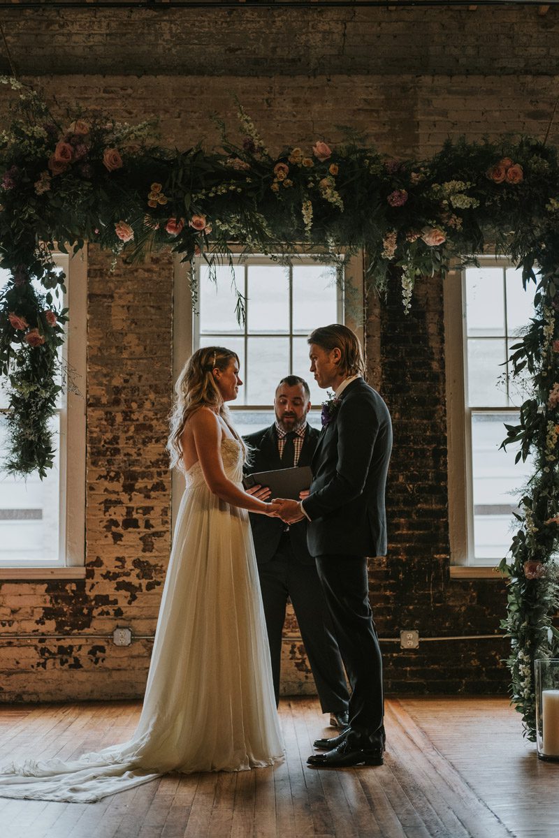 Bride and groom hold hands under arbor at The Stockroom at 230, Hartman Outdoor